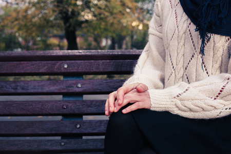 A young woman is sitting on a park bench on a sunny day in autumnの写真素材