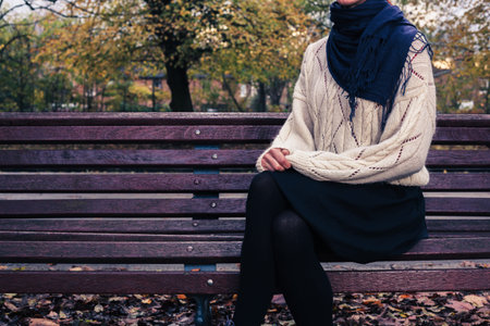 A young woman is sitting on a park bench on a sunny day in autumn