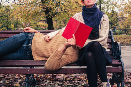 A young couple is reading and relaxing on a park bench in autumnの写真素材
