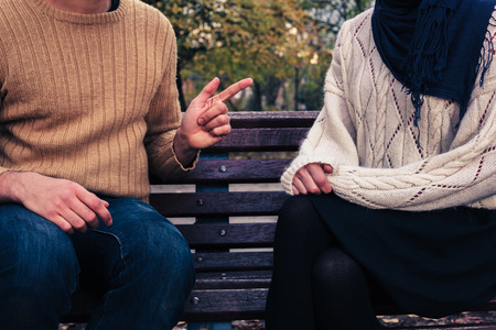 A young man and woman are sitting on a park bench and arguingの写真素材