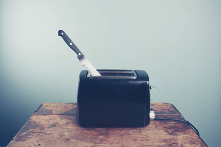 An electric toaster on a wooden table with a bread knife in it