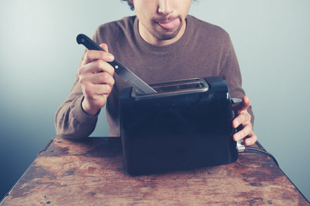 A silly young man is sticking a knife into an electric toaster