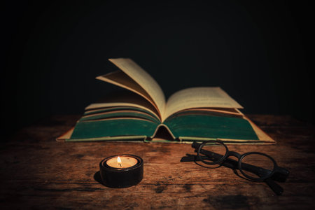 An open book and some glasses at night by candle lightの写真素材