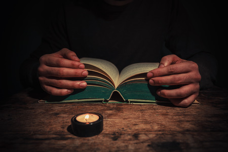 A man is reading a big book by candle light at nightの写真素材
