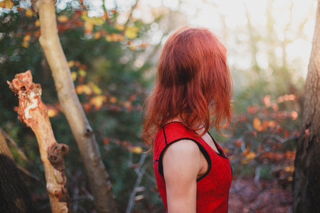 A young woman wearing a red dress is standing in the forest on a sunny winter dayの写真素材