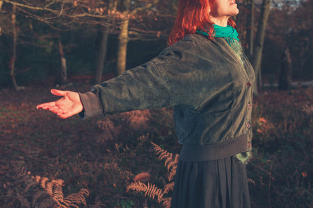 A young woman is raising her arms in joy as she is standing in a forest at sunset