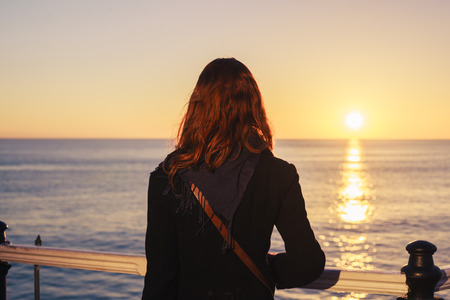 A young woman is walking on the coast at sunset and is admiring the seaの写真素材