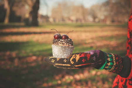 A gloved hand is holding a cupcake with a cherry on topの写真素材