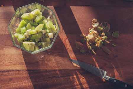 A bowl of kiwi slices and a knife on a wooden chopping boardの写真素材
