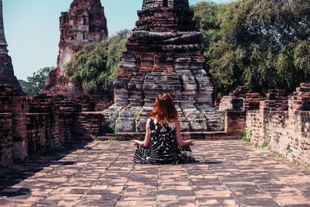 A young woman is sitting and meditating amongst the ruins of an ancient buddhist templeの写真素材
