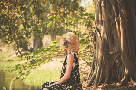 A young woman is sitting under a tree by the riverの写真素材