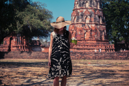 A young woman is drinking juice from a coconut near the ruins of an ancient buddhist templeの写真素材