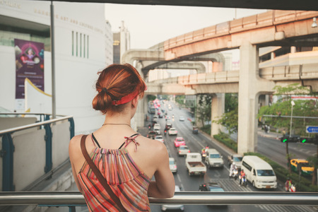 A young woman is looking at the traffic from an overpass in Bangkokの写真素材