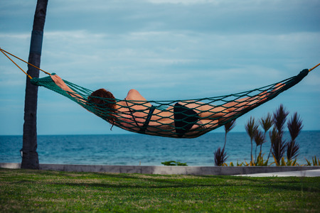 A young woman is relaxing in a hammock by the seaの写真素材