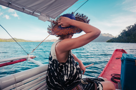 A young woman wearing a hat is on a boat in the tropicsの写真素材