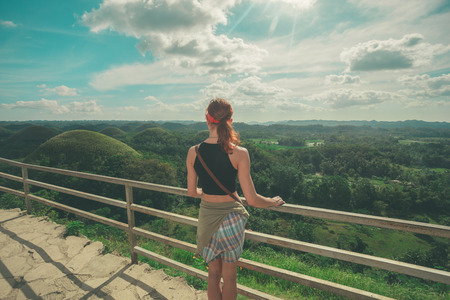 A young woman is standing and admiring the view of the famous Chocolate hills in Bohol, Philippinesの写真素材
