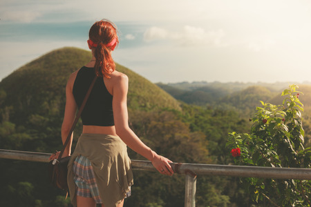 A young woman is standing and admiring the view of the famous Chocolate hills in Bohol, Philippinesの写真素材