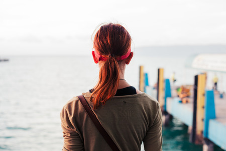 Rear view of a young woman standing by a pier at sunsetの写真素材