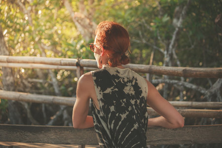 A young woman is sitting on a bench in the jungle at sunset
