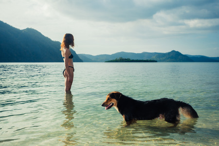 A young woman in a swimsuit is standing on a tropical beach with a dogの写真素材