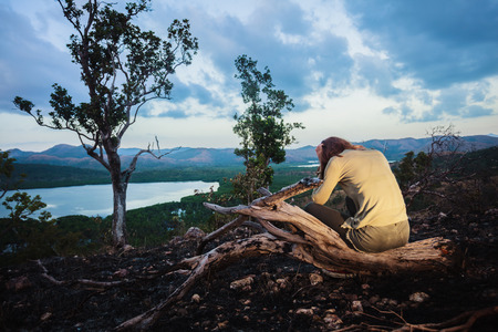 A sad young woman is sitting on a hill burned by a wild fireの写真素材