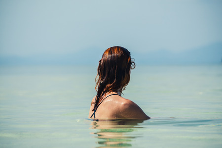 A young woman is sitting in the water by a tropical beachの写真素材