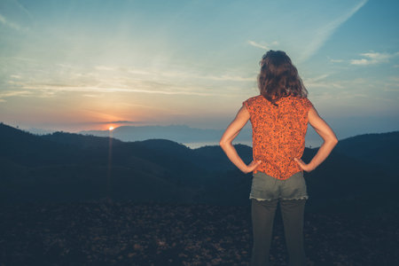 A young happy woman is watching the sunrise over the mountains in a tropical country