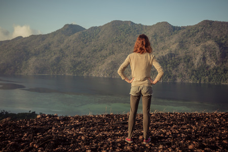 A young woman is standing on a mountain overlooking a bayの写真素材
