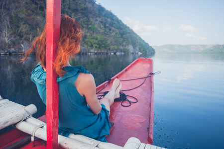 A young woman is relaxing on the bow of a small boat in a tropical climate