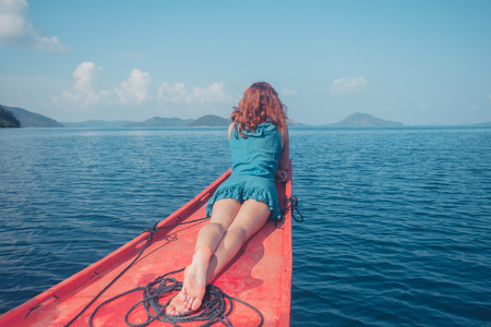 A young woman is relaxing on the bow of a small boat in a tropical climateの写真素材