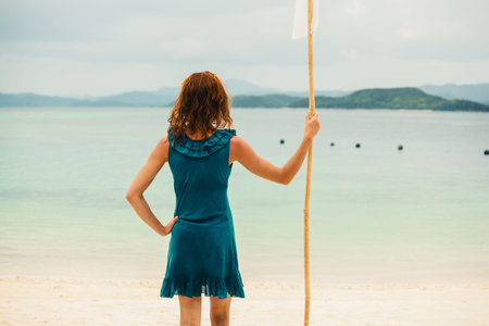 A young woman is standing on a tropical beach and is holding a  white flag