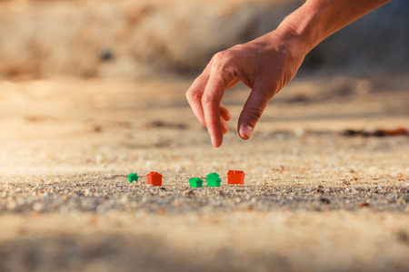 A hand is picking up a small plastic house on the beachの写真素材