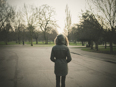 A person wearing a warm coat with a big hood is standing in a park at sunsetの写真素材