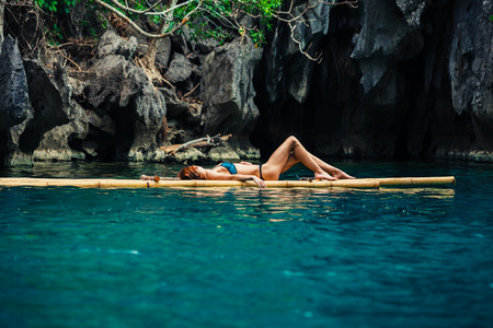 A beautiful young woman in a swimsuit is relaxing on a bamboo raft in a tropical lagoonの写真素材