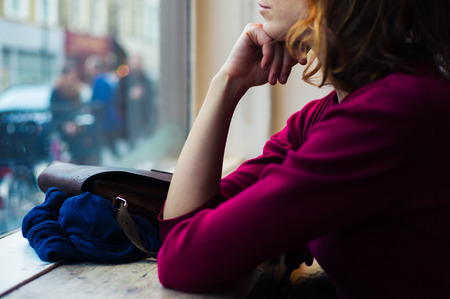 A young woman is sitting by a window and is looking out and day dreamingの写真素材