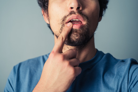 Confused young man touching his lip with his fingerの写真素材