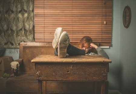 A young woman wearing worn out shoes is resting her feet on a table at homeの写真素材
