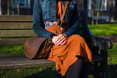 A young woman is sitting on a bench with houses in the backgroundの写真素材