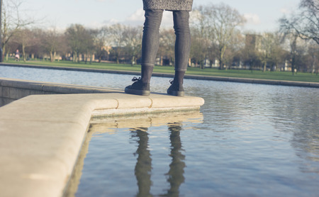 The legs of a young woman standing by the water of a fountain in a parkの写真素材
