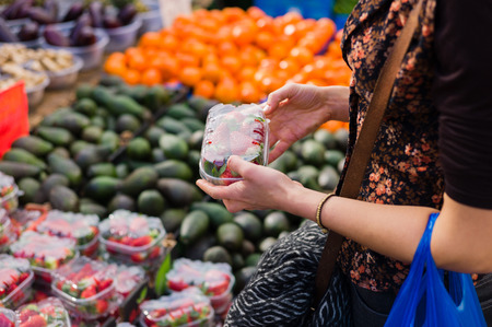 A young woman is at a fruit and vegetable market and is hoding a box of strawberriesの写真素材