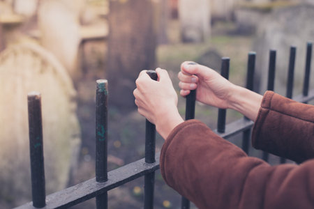 A pair of hands are holding a fence surrounding a graveyard