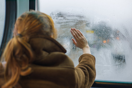A young woman is wiping the dew off a window in a busの写真素材