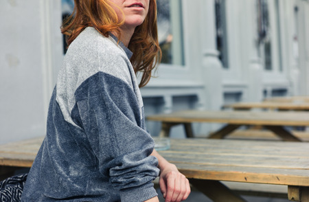 A young woman is sitting on a bench outside a pub or restaurant on a day in springの写真素材