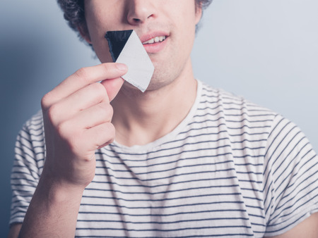 A young man is removing a piece of tape that has been covering his mouthの写真素材