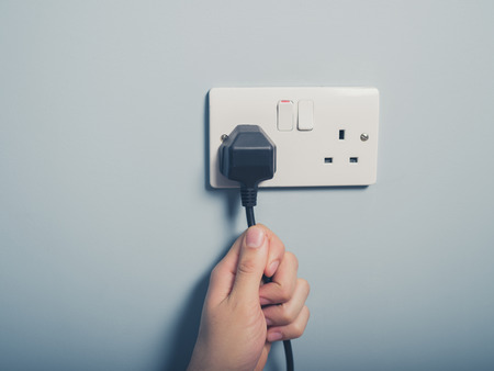 A male hand is pulling an electrical cord plugged into a wall socketの写真素材