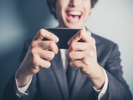 A happy young businessman is laughing about something on his smartphoneの写真素材