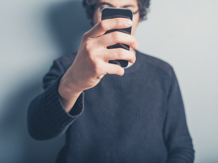A young man is taking a selfie of himself using his smartphoneの写真素材