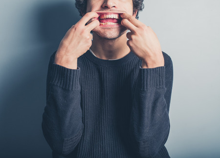 A young man wearing a black sweater is pulling silly facesの写真素材