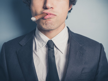 A young confident businessman is smoking a cigarの写真素材