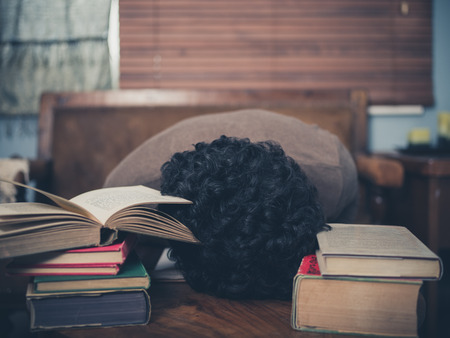 A tired student is asleep with his head on a coffee table surrounded by booksの写真素材